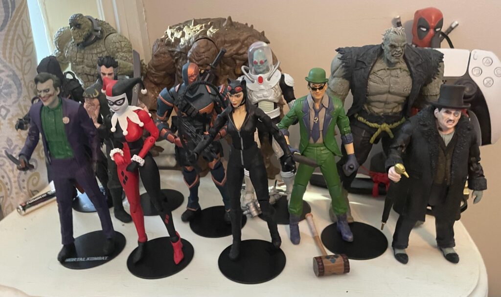 Coleção de action figures da DC, com Batman, Coringa e Arlequina em destaque, mostrando a riqueza de detalhes e a atmosfera sombria dos personagens.